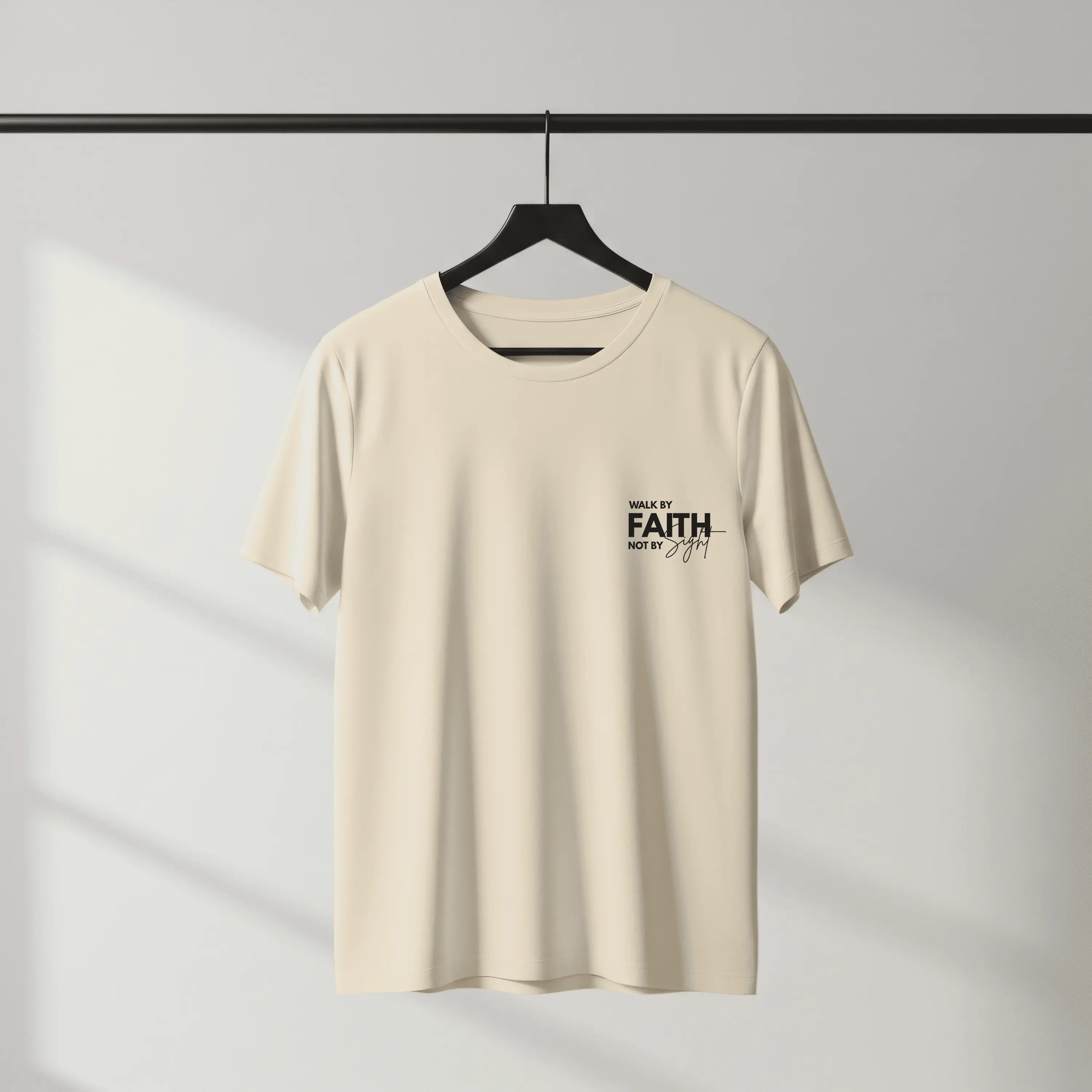 Beige t-shirt with 'Walk by Faith, Not by Sight' text on a hanger against a gray background